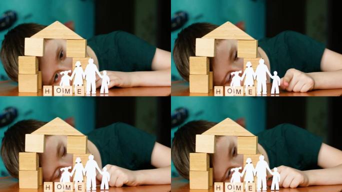 肖像快乐的高加索孩子扮演剪纸家庭，用木制立方体建造房屋。这个男孩梦想着一个家庭和一个家。玩积木的孩子