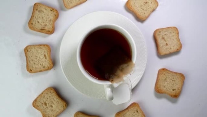 一杯茶，茶包和许多白色脆皮饼干在浅色背景下缓慢旋转。