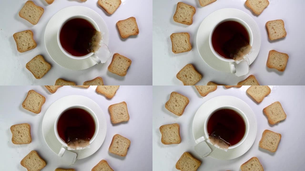 一杯茶，茶包和许多白色脆皮饼干在浅色背景下缓慢旋转。