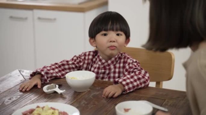 当他的母亲在餐桌上用叉子喂他一块肉时，可爱的亚洲小男孩有选择性地张开嘴的慢动作。