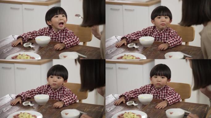 当他的母亲在餐桌上用叉子喂他一块肉时，可爱的亚洲小男孩有选择性地张开嘴的慢动作。