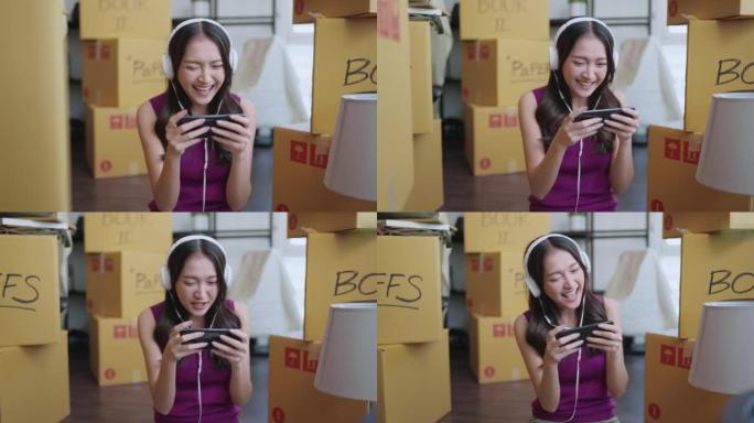 快乐的笑容，一边打包回家在公寓搬家，亚洲女性成人手在智能手机上玩网络游戏，一边打包东西，一边搬家房蓬