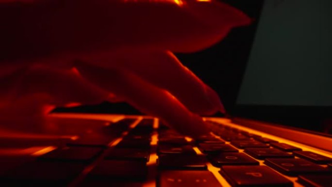 在黑暗的办公室里，用红灯在笔记本电脑键盘上打字的女性手的低角度镜头。在笔记本上工作的女性。自由职业者