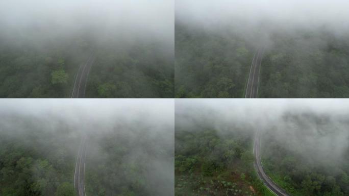 空中无人机电影拍摄的汽车和道路在早上下雨后越过山顶，有雾和绿色森林。