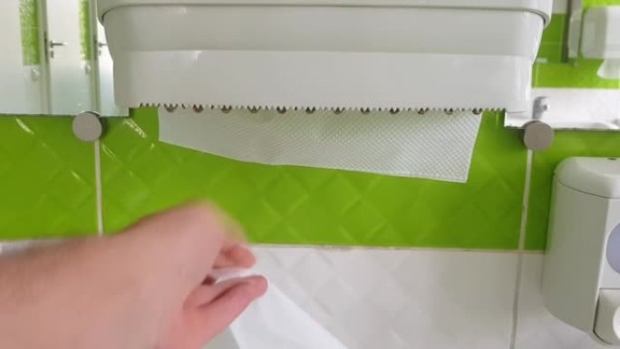 一名男子用手从公共厕所的白色塑料盒中拉出纸巾。第一个人的视频。该男子的手拉出一张纸擦拭湿手。医疗保健