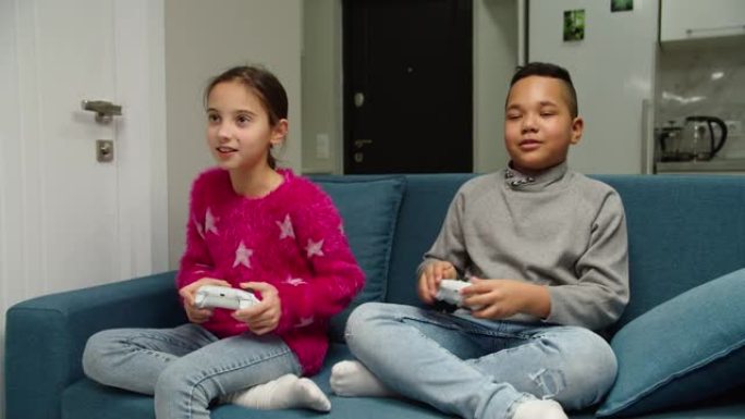 多民族男孩和女孩玩电子游戏，坐在室内的沙发上