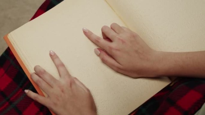 盲人妇女阅读盲文书籍的俯视图，看不见的女性学习阅读，残疾人的家庭教育，在纸上触摸字母。