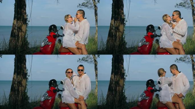 在森林之路之旅中，穿着白色衣服的红色摩托车上的爱情情侣。两名白人旅游妇女和男子亲吻拥抱坐在踏板车上