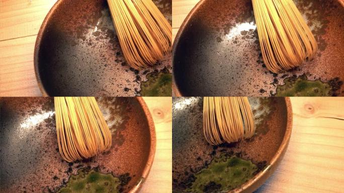 在带有斑点绿色珐琅的棕色陶瓷碗中，由分裂的竹子制成的日本茶搅拌器的宏观