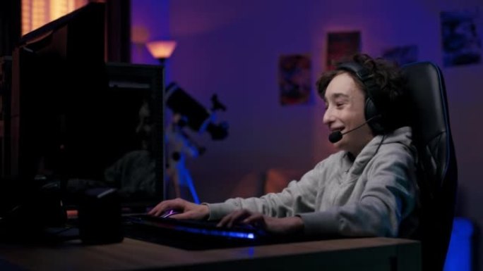 带耳机的小玩家，男孩深夜坐在电脑显示器前，和他的团队玩多人射击视频游戏，房间被led灯照亮