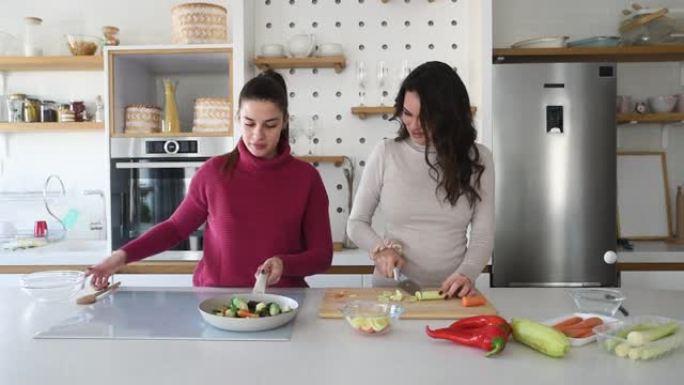两个年轻快乐的大学生室友或商务女性在他们的公寓里一起做饭。女性在舒适的家中一起在现代厨房做饭很开心。
