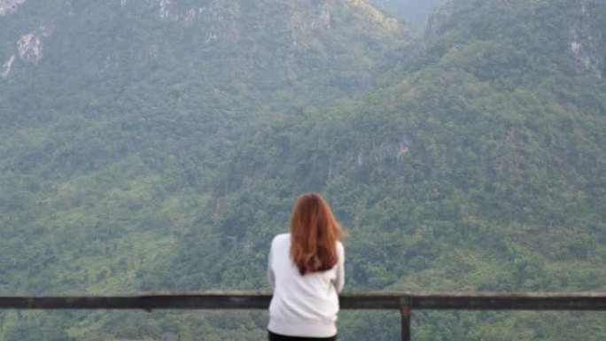 一位女性旅行者坐在木制阳台上看着美丽的山景的模糊后视图