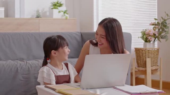 亚洲年轻的母亲和她的女儿用电脑笔记本电脑一起看网络媒体或电影。幸福妈妈和小女孩看着笔记本电脑微笑和大