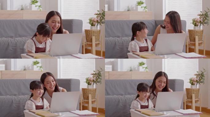 亚洲年轻的母亲和她的女儿用电脑笔记本电脑一起看网络媒体或电影。幸福妈妈和小女孩看着笔记本电脑微笑和大