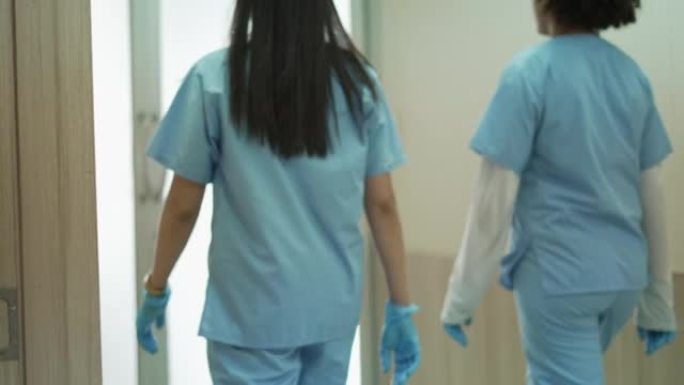 后视图。专业团队的外科医生或医生和护士穿着医袍，走进手术室，在无菌手术室为手术病人做准备。概念医院，
