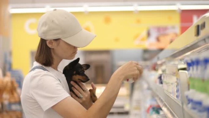 年轻女子手里拿着小狗在超市购物。