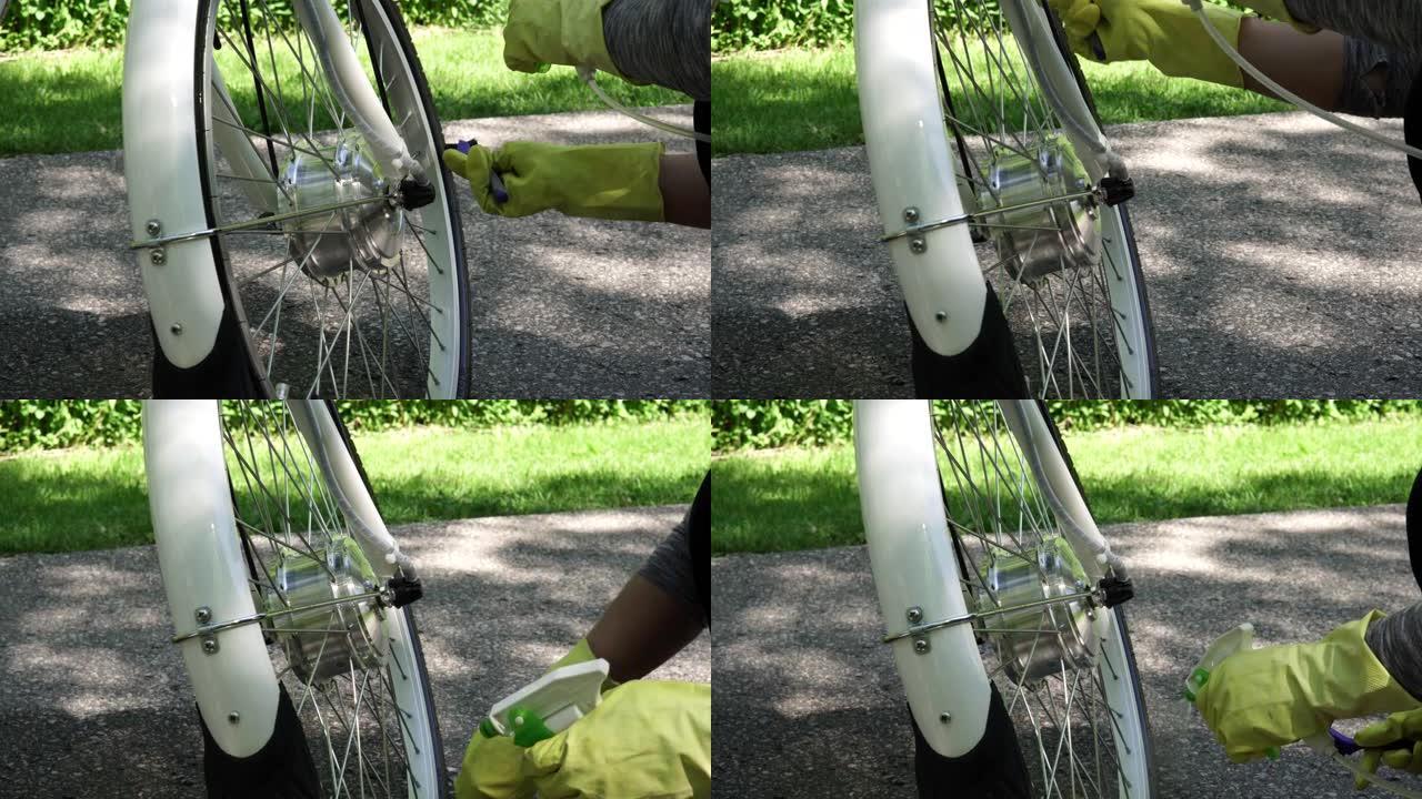 戴黄色手套的骑自行车的人在夏天在外面喷水清洁电动自行车电动轮的轮胎。骑手照顾带电机的运动电动自行车车