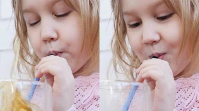 一个孩子一个少年一个女孩从玻璃杯中的可重复使用的吸管中喝水果饮料，并通过向玻璃杯中吹气来调皮，结果发