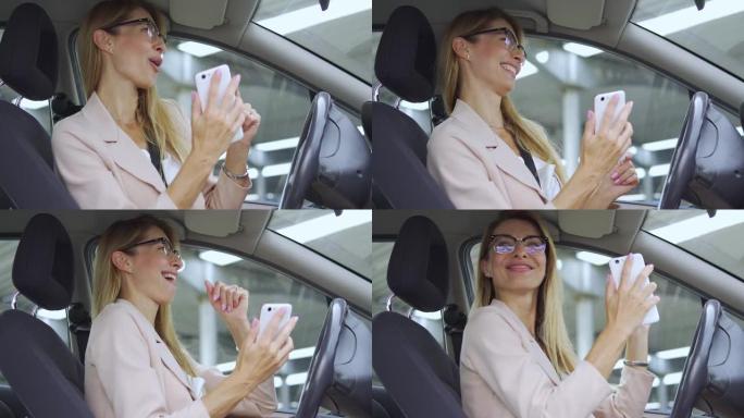美丽兴奋的金发女人，穿着优雅的轻便西装，积极走向最喜欢的歌曲的节奏，坐在车里的智能手机上听音乐，积极
