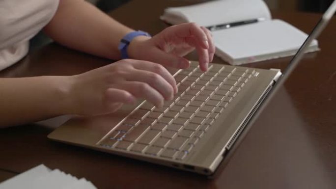 女性的手正在笔记本电脑键盘上打字。手指快速地按下键盘上的键。在它旁边有一个笔记本。个人电脑，在家远程
