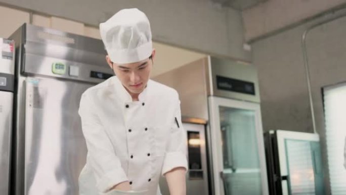 面带微笑的面包师看着相机 .. 厨师贝克穿着厨师的衣服和帽子，在厨房里一起做饭。年轻的亚洲人从厨房的