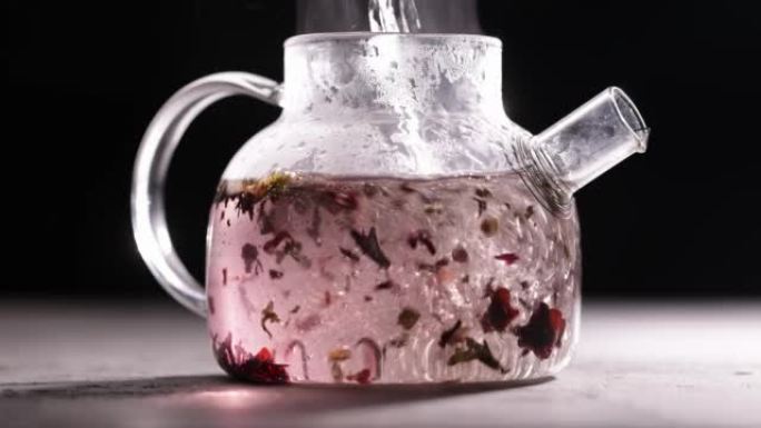 在深色背景下的玻璃透明茶壶中冲泡红茶的过程。将热水倒入带茶叶的水壶中。