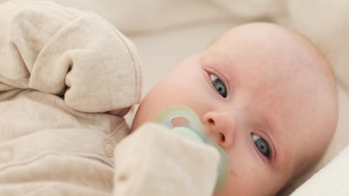 一个可爱的婴儿的肖像，嘴里叼着奶嘴，躺在白色的毯子上，穿着白色的衣服，抽泣着