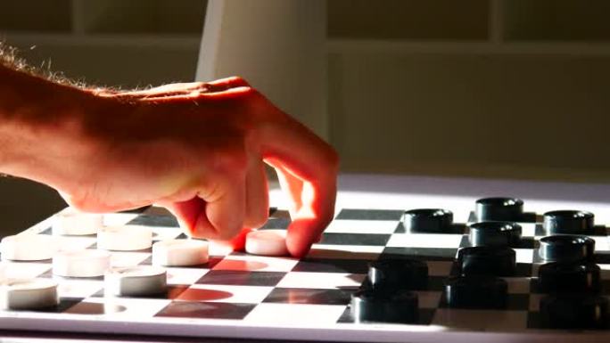 跳棋棋盘的特写镜头和一个男人的手砍下了一个黑色的跳棋