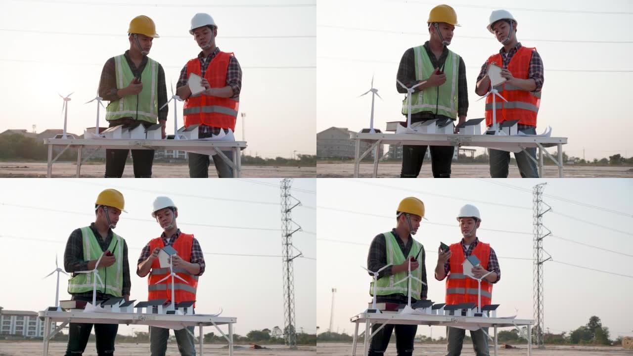 两名电气工程师在建筑工地项目中讨论家用太阳能电池农场和风力涡轮机模型，并在日落时讨论高压电力线塔。团