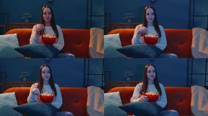 女人独自坐在沙发上，吃爆米花，在家看有趣的电视连续剧，恐怖片