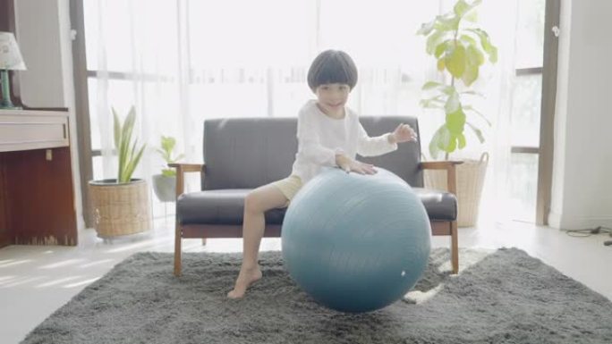 微笑可爱的男孩在玩耍的时候快乐，在家休闲。亚洲小男孩在现代客厅玩瑜伽球轻功。假日家庭活动，在家上学，