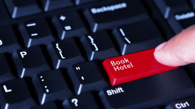 特写一名男性手指按下电脑键盘上红色的图书酒店按钮