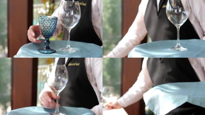 精英餐厅的餐桌设置特写。男人的手布置漂亮干净的空玻璃玻璃杯和盘子。装饰餐具和烛台。服务员摆桌子