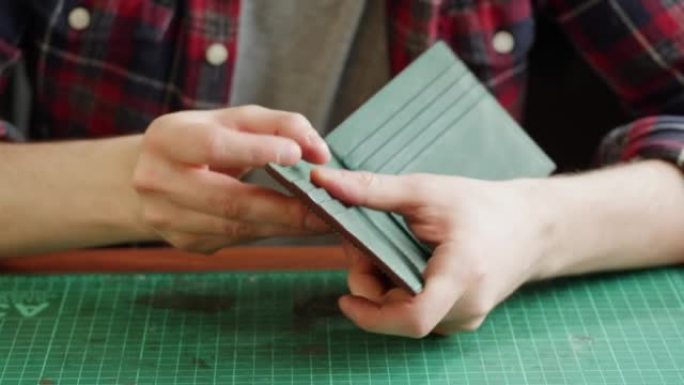 人造皮革特写制作的男士裁缝修复钱包。工匠在工作场所餐桌上制作手工配件。专业工作室。