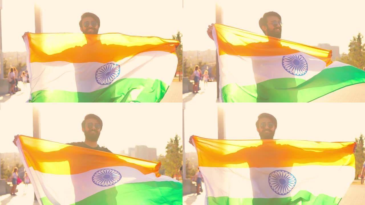 英俊的印度大胡子男子，穿着黑色棉t恤，在夏日公园的夕阳下挥舞着印度国旗。