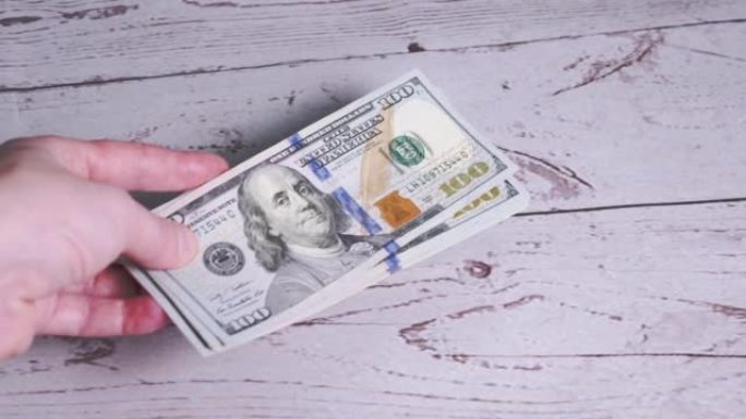 女性的手把一叠100美元的钞票放在桌子上。4K.特写