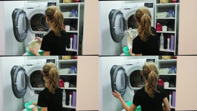 一个女人把衣服放在洗衣机里。洗衣房内部。
