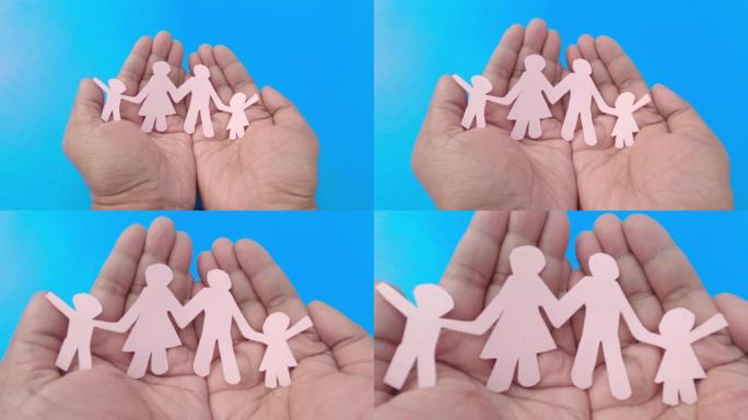 快乐纸家庭在一个男人的手上，手掌朝上，蓝色背景。放大。折纸工艺装饰形状和人物。