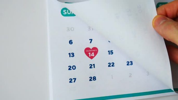一只男性手的特写镜头翻过挂历的2月页，然后是下一页，上面标有粉红色心形符号的情人节日期