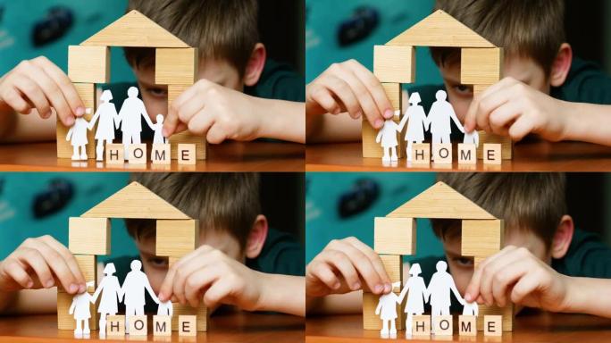一个快乐的孩子玩积木，盖起了房子，把碑文做成了家。一名高加索学龄前儿童从纸上剪下家庭剪影，在家玩耍。