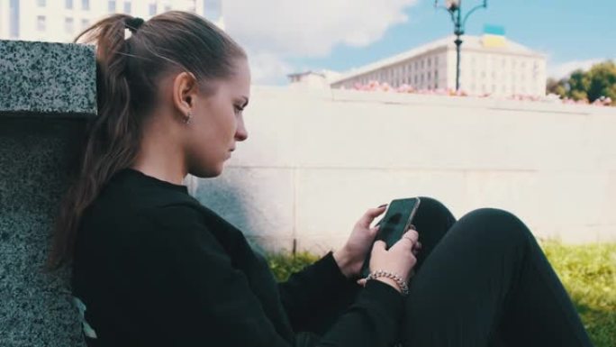 年轻女子坐在街头公园的栏杆上时使用智能手机