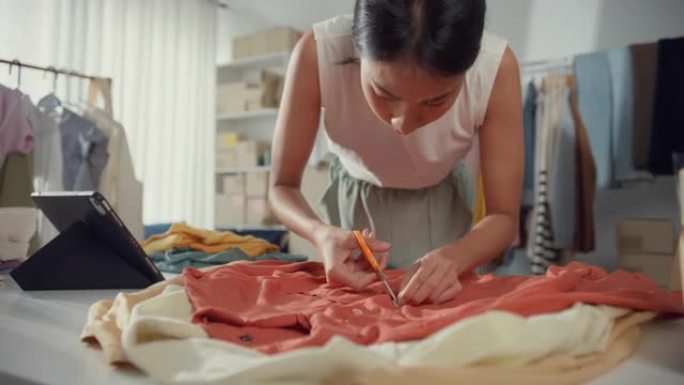 年轻的亚洲小企业主妇女准备包装订单衬衫产品发送给客户，并在家里的平板电脑上检查库存。