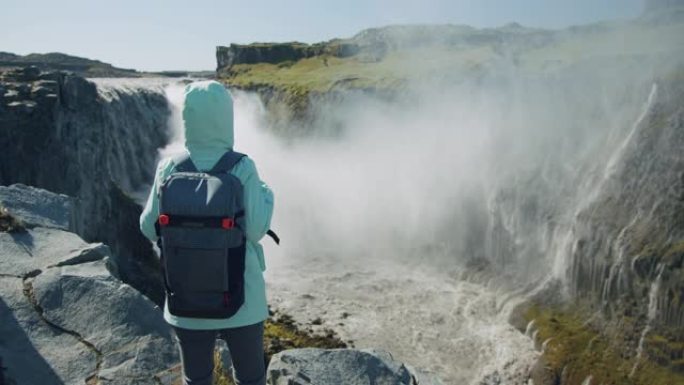 穿着夹克和背包的女人站在悬崖边看着冰岛的Detifoss瀑布