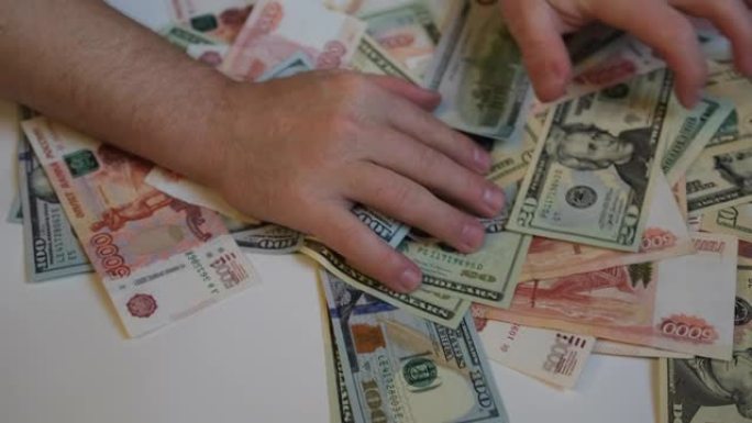 男人的手从俄罗斯和美国的钞票上扒出一堆钱，特写镜头。