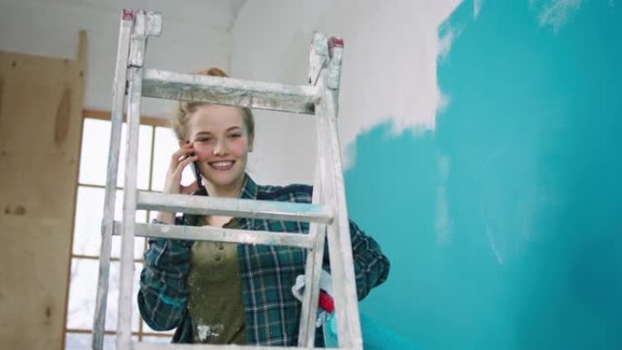 微笑的大美丽的女人，一边粉刷墙壁，站在秤上，拿起电话打个电话，她和某人说话