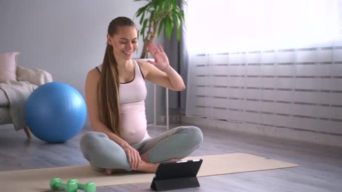 孕妇坐在公寓房间的地板上练习瑜伽和使用平板电脑