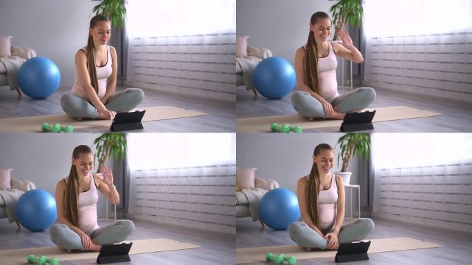 孕妇坐在公寓房间的地板上练习瑜伽和使用平板电脑