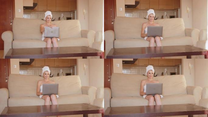 穿着浴巾的女人在沙发上使用无线笔记本电脑
