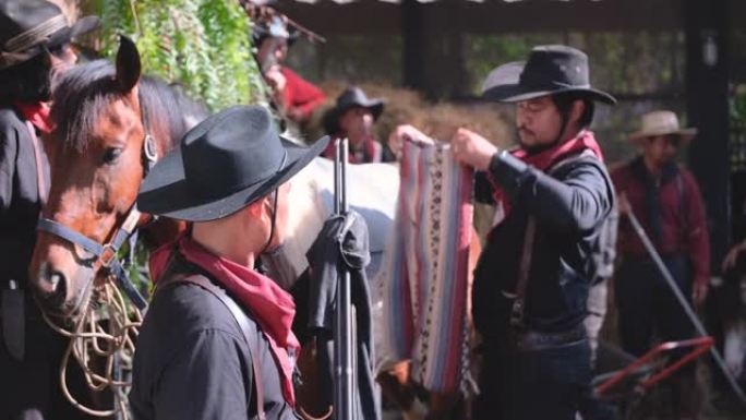 牛仔男子的肖像用其他布在马背上清洁长枪，有人清洁稳定区域