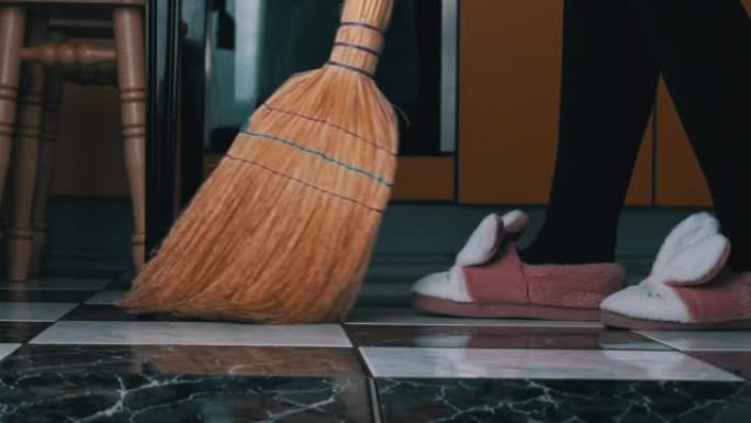 年轻女孩用普通的扫帚在厨房里扫地板